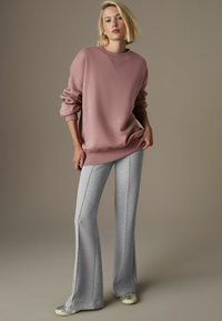 Różowy, oversize sweter z okrągłym dekoltem, skomponowany z szarymi spodniami dresowymi w fasonie dzwonów, charakteryzującymi się teksturowanym wykończeniem i bocznymi szwami.