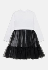 Pitkähihaista mekkoa, jossa on valkoinen puuvillapaita ja musta organza-hame, jonka helma on röyhelöinen, yhdistäen pehmeän kankaan ja läpikuultavan tekstuurin.