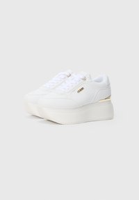 Άσπρα platform sneakers με υφή υφάσματος, επίπεδα κορδόνια και χρυσή λεπτομέρεια στη φτέρνα. Το λογότυπο της μάρκας εμφανίζεται στο πλάι.