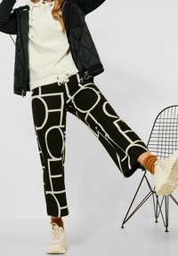 Sorte og beige mønstrede bukser med geometriske designs, med elastik i taljen og en cropped pasform, parret med en let top og sneakers.