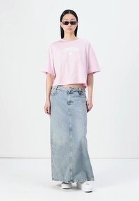 Lyserød cropped t-shirt med "Converse" logo, kombineret med en lang denimnederdel i lys blå. Modellen bærer små solbriller og hvide sko.
