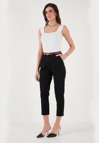 Top senza maniche bianco a collo quadrato, pantaloni neri a vita alta con tasche, cintura marrone e décolleté beige con punta nera. Stile semplice e sartoriale.