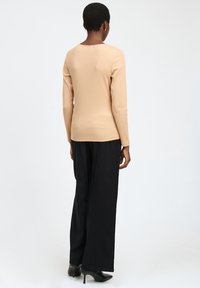 Top beige de manga larga con cuello redondo y textura acanalada, combinado con pantalones negros de pierna ancha y tacones de aguja, visto desde atrás.