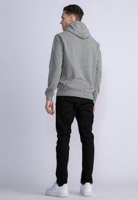 Sudadera con capucha gris de corte relajado, textura suave y puños de canalé, combinada con pantalones negros y zapatillas blancas.