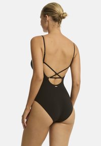 Czarny jednoczęściowy strój kąpielowy z cienkimi, regulowanymi ramiączkami, o okrągłym dekolcie na plecach, z krzyżującymi się detalami oraz małym metalicznym logo z tyłu.