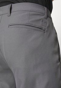 Gray athletic pants made of smooth fabric, featuring a back pocket and a small logo patch. Sleek design with a tailored fit.