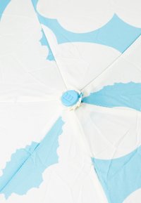 Umbrella featuring a white canopy with a blue wave pattern, central button, and ribbed edge. Material shows light texture and folds.