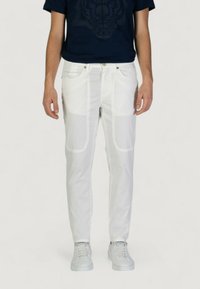 Pantaloni bianchi a taglio slim, con tasche laterali e cuciture in vista. Abbinati a una maglietta blu navy e sneaker bianche.