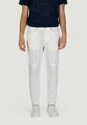 Pantaloni bianchi a taglio slim, con tasche laterali e cuciture in vista. Abbinati a una maglietta blu navy e sneaker bianche.