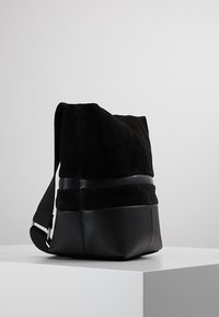 Czarna torba wykonana z zamszu i skóry, o miękkiej fakturze, prostokątnym kształcie i regulowanym pasku. Minimalistyczny design bez widocznego okucia.