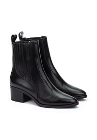 Botas de cuero negro hasta el tobillo con punteras puntiagudas, paneles laterales elásticos y un tacón bajo estilo bloque. Asa distintiva en la parte posterior para facilitar su uso.