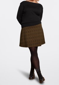 Svart tröja med båtkrage, kombinerad med en brun mönstrad kjol med vågmönster. Bärs med svarta snörboots och strumpbyxor.