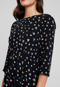 Schwarzes Kleid mit floralem Muster in Pink, Gelb und Weiß, mit Dreiviertelärmeln und gerafftem Taillendetail. Glatte Textur.