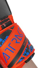 Red fabric strap with blue text and graphic pattern, featuring black accents and a woven texture, attached to a black surface.
