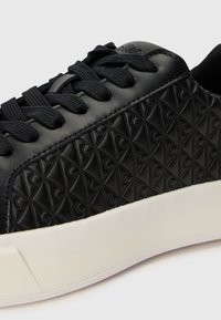 Sneaker in pelle nera con motivo a rombi in rilievo sui lati, lacci piatti e suola in gomma bianca. Logo discreto sulla linguetta.