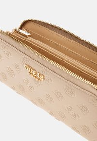 Beige nahkrahakott, millel on reljeefne logo muster, kuldne metalldetail ja lukuga sulgemine. Siseosa sisaldab mitmeid sektsioone korralduse jaoks.
