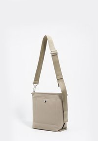 Beżowa torba na ramię z fakturowaną powierzchnią, regulowanym materiałowym paskiem, przednią kieszenią oraz wyraźnym srebrnym akcentem metalowym.