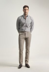 Camisa de botones gris claro con mangas largas, combinada con pantalones beige claros y mocasines marrones, mostrando un ajuste ordenado y a medida.
