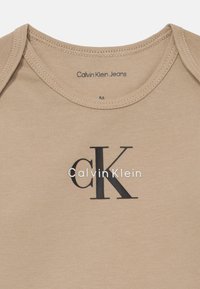 Μωρό φορμάκι Calvin Klein Jeans σε μπεζ χρώμα με λογότυπο "cK Calvin Klein" σε μαύρο και άσπρο τυπωμένο μπροστά.