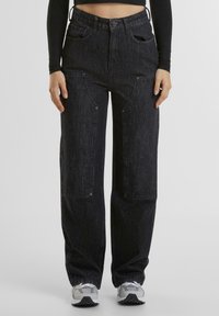Pantaloni in denim neri con una vestibilità rilassata, dotati di ampie tasche frontali, dettagli di cucitura a vista e un design a vita alta.
