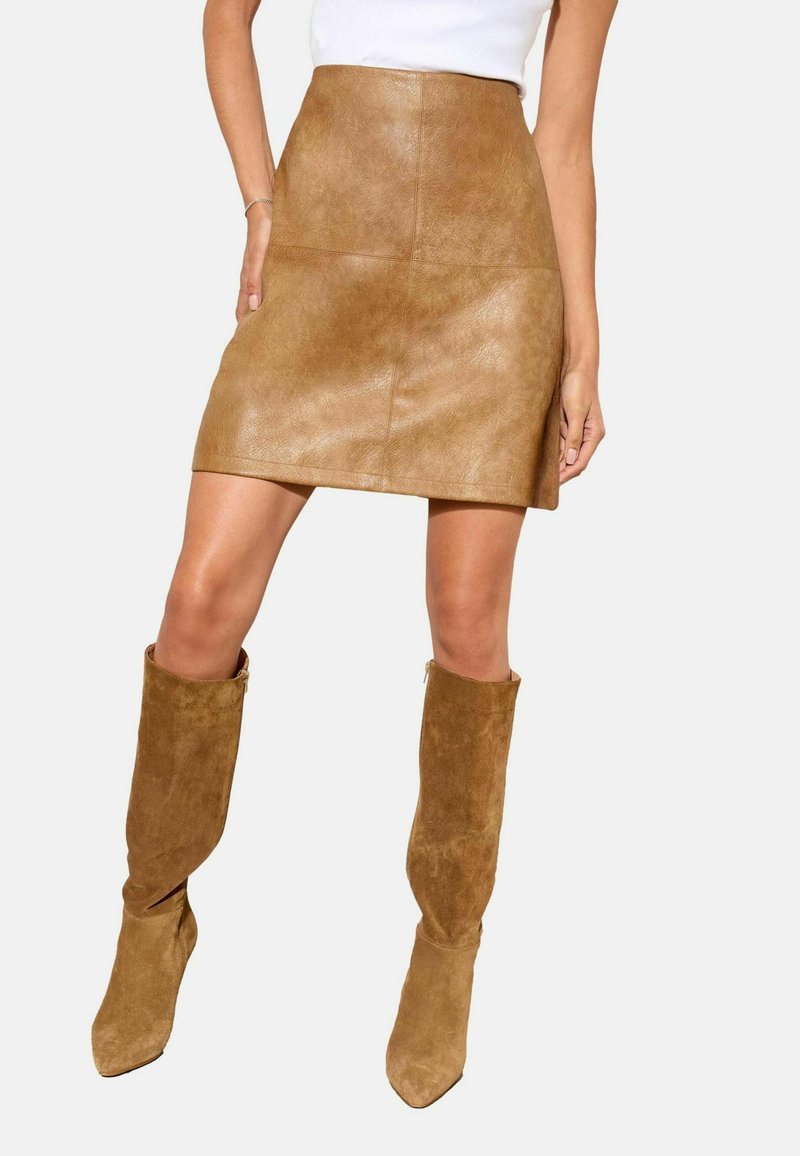 Pruun nahkmini seelik, sile tekstuur ja paneeli detailidega. Kombineeritud kuni põlveni ulatuvate pruuni suede saapadega, millel on terav nina.