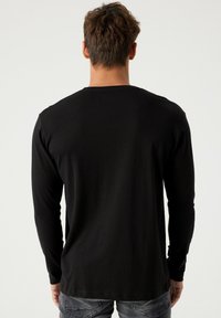 Camiseta negra de manga larga hecha de tejido suave, con un escote redondo y mangas ajustadas, mostrada desde la parte posterior.
