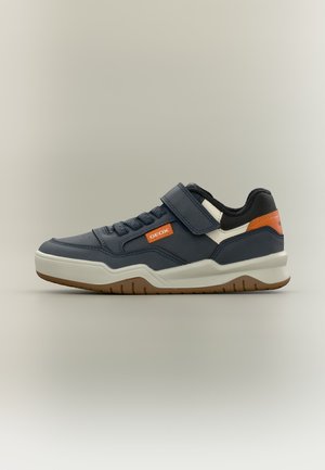Baskets bleu marine avec semelle blanche, accents orange, bande velcro et lacets, vue de côté sur un fond uni clair.