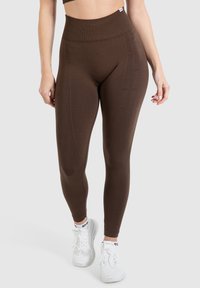 Bruine high-waisted leggings van rekbare stof, met een naadloos ontwerp en subtiele textuur. Draag ze met witte sportschoenen.