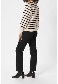 Beige raidoilla varustettu neulepaita puhvihihnoilla, yhdistettynä mustiin suoriin housuihin ja mustiin nilkkabootseihin. Sileä kangas ja istuva siluetti.