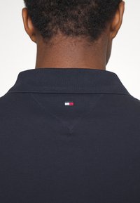Marineblauw polo shirt van een gestructureerde brei stof, met een klein rood, wit en blauw logo aan de achterkant van de kraag.
