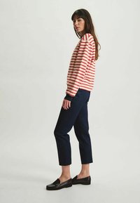 Chemise à rayures rouges et blanches à manches longues associée à un pantalon cropped bleu marine et des chaussures noires à enfiler. Design simple, coupe décontractée.