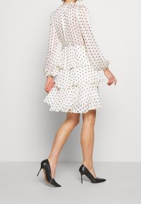 Vestido blanco con lunares, con capas de volantes, tela transparente y mangas largas, combinado con zapatos de tacón negros. Diseño simple con una textura delicada.