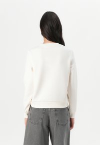 Kremfarget sweatshirt med rund hals, ribbede mansjetter og fald, kombinert med middels grå vide jeans med baklommer.