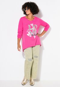 Chemise rose à manches longues avec un graphique "LOVE" en noir et imprimé léopard, associée à un pantalon large vert clair et des bottes métalliques dorées.
