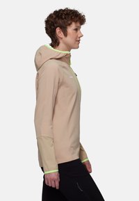 Leichte beige Kapuzenjacke aus strukturiertem Stoff mit leuchtend grünen Akzenten und elastischen Bündchen, entworfen für Outdoor-Aktivitäten.