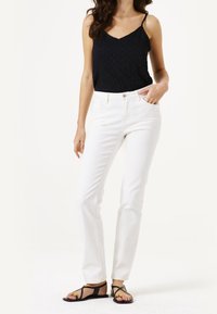 Bílé rovné džíny se pěti kapsami, spárované s černým texturovaným topem na ramínka. Modelka má na sobě černé ploché sandály.