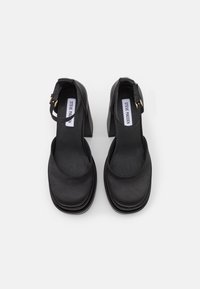 Chaussures noires à talon ouvert avec un talon bloc épais, présentant une finition en cuir lisse, une bride à la cheville et une semelle intérieure rembourrée.