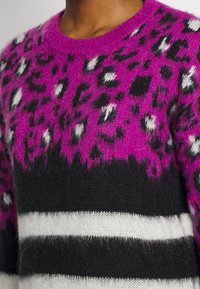 Sweater featuring a pink and black leopard print design, with white stripes at the bottom. Made from soft, textured fabric.