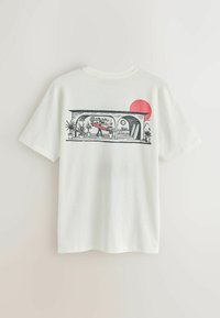 T-shirt blanc avec un graphisme d'un surfeur portant une planche de surf rouge à l'intérieur d'une véranda avec des plantes et des planches de surf, soleil rouge en arrière-plan.