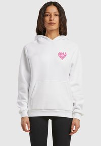 Biela mikina vyrobená z bavlny, s prednou vreckom a ružovým srdcovým grafickým motívom s textom "MÁŠ SKVELÝ DEŇ" na hrudi.