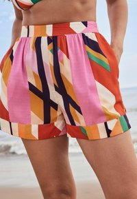 Kraťasy v mnoha barvách s geometrickými vzory v růžové, oranžové a černé barvě. Vyrobeny z hladkého materiálu s nařaseným pasem a bočními kapsami.