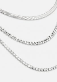 Tre sølvhalskæder: et fladt slangekæde, et kædedesign med led og et med cubic zirconia-accenter, der viser forskellige teksturer og designs.