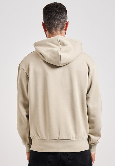 Felpa con cappuccio beige dalla vestibilità rilassata, con polsini e orlo a coste. Texture liscia e design semplice; senza motivi o loghi visibili.