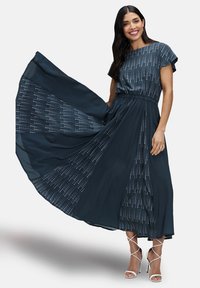 Navyblauwe maxi-jurk met korte mouwen, voorzien van een gestructureerd patroon van lichte stippen. Vloeiende stof met een elastische tailleband en enkel-lange lengte.