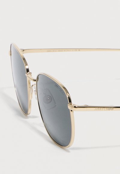 Γυαλιά ηλίου aviator με χρυσή κορνίζα, σκουρόχρωμους φακούς και το λογότυπο "Jimmy Choo" στον φακό και το πλαίσιο, πάνω σε λευκό φόντο.