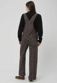 Salopette à imprimé léopard dans des tons foncés, avec une coupe ample, des jambes larges et des bretelles croisées dans le dos. Fabriquée en tissu texturé.