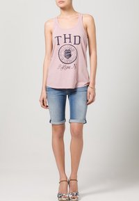 Top sin mangas rosa con estampado gráfico marino, combinado con pantalones cortos de denim azul claro doblados en el dobladillo, y sandalias de tacón alto con estampado floral.