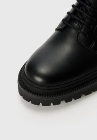 Černá kožená kotníková bota s texturovanou špičkou a silnou gumovou podrážkou, se šněrovacím designem a zesílenými švy.