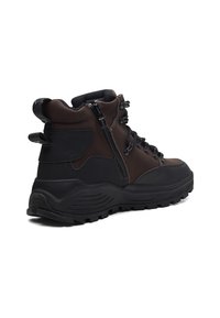 Bruine wandelschoenen met een zwarte rubberen zool, zijrits en vetersluiting aan de voorkant. Beschikt over versterkte enkelondersteuning en textuuraccenten van stof.