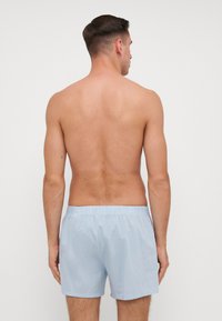 Pantaloni da bagno azzurri con vita elastica, caratterizzati da una texture liscia e una vestibilità comoda, mostrati da dietro su un torso nudo.